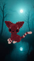 BrainRotPop handmade burgundy crocheted plush creature with white stitched details and large dark eyes in a forest.