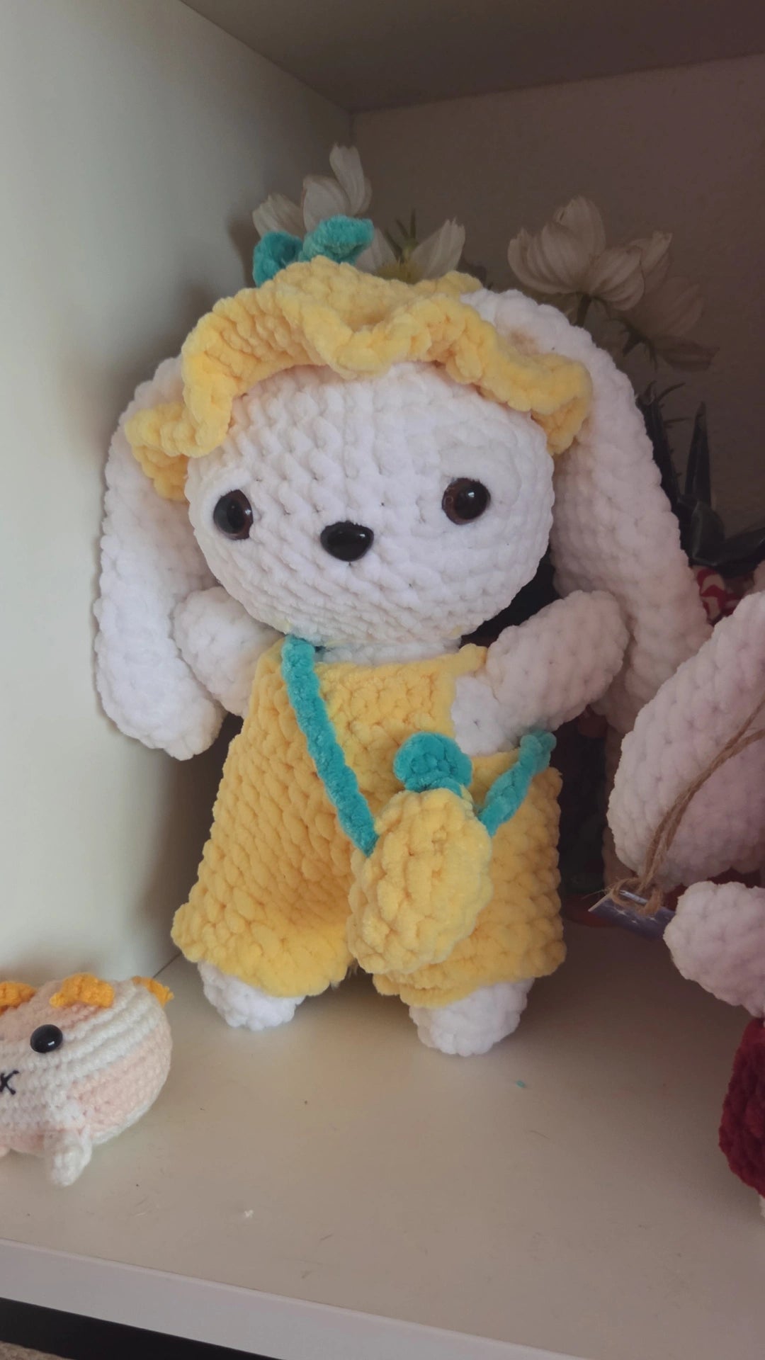 BrainRotPop handmade white crochet bunny plushie wearing a yellow sun hat, yellow dungarees, and a teal cross-body bag.