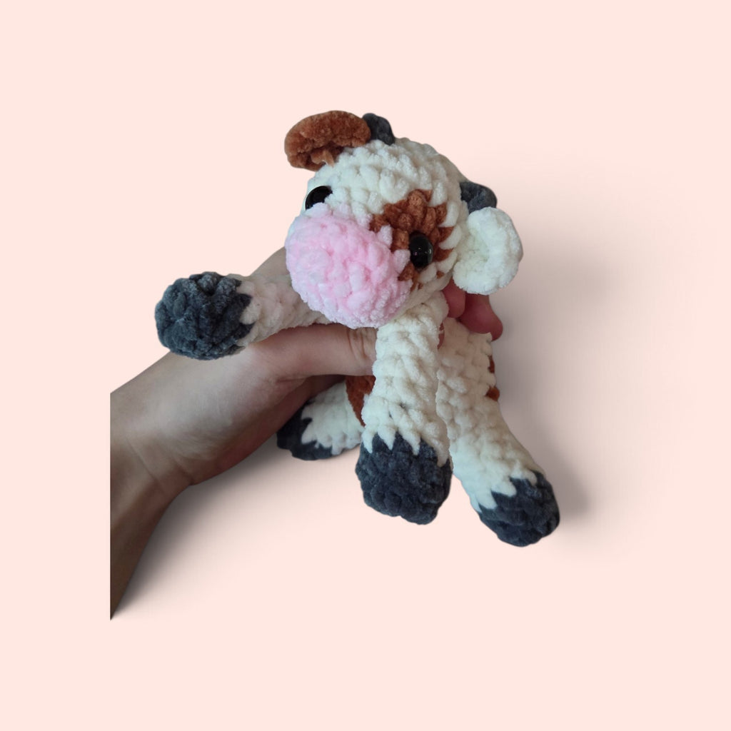 BrainRotPop handmade crochet cow plush toy in cream, brown, and pink soft chenille yarn held in a hand.