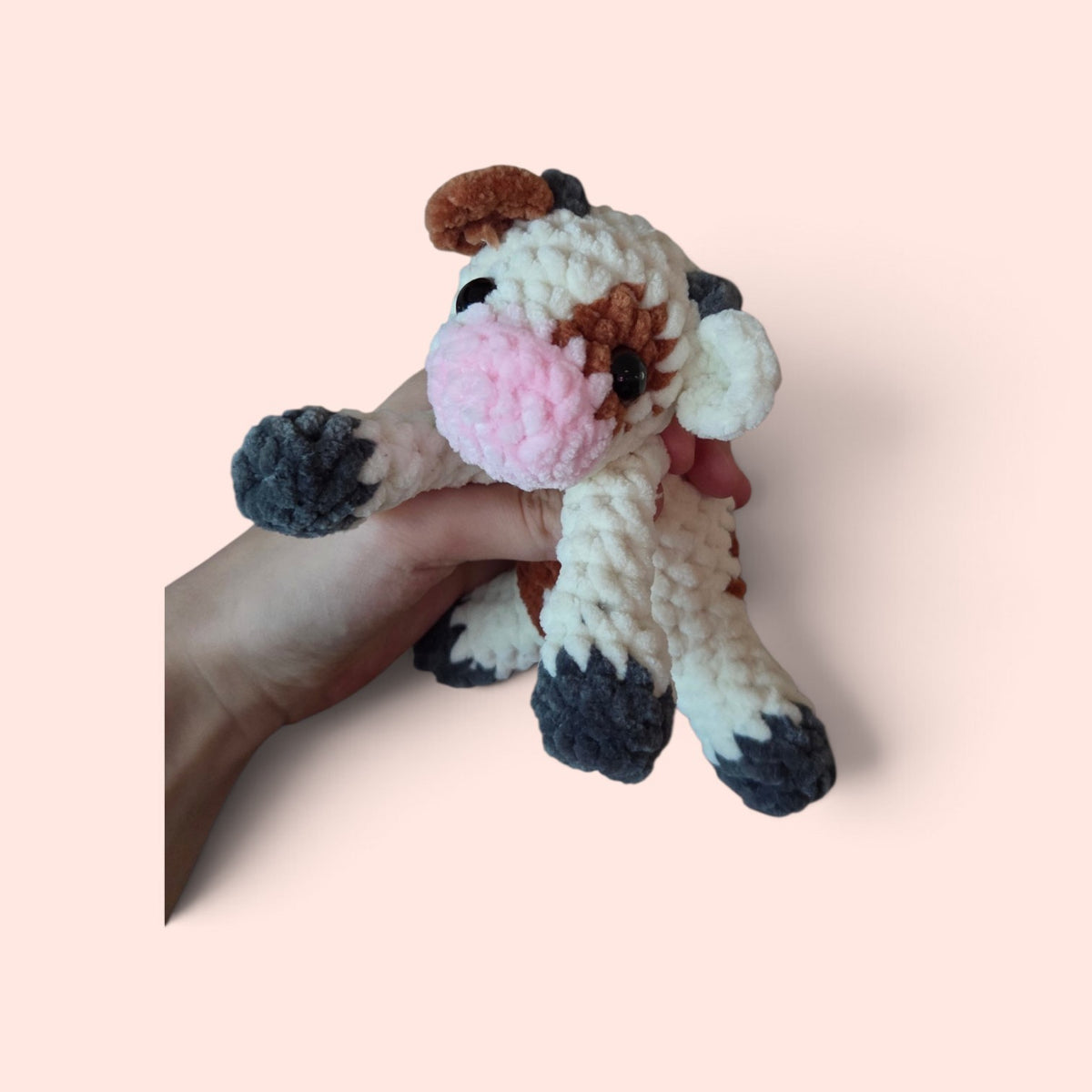 BrainRotPop handmade crochet cow plush toy in cream, brown, and pink soft chenille yarn held in a hand.
