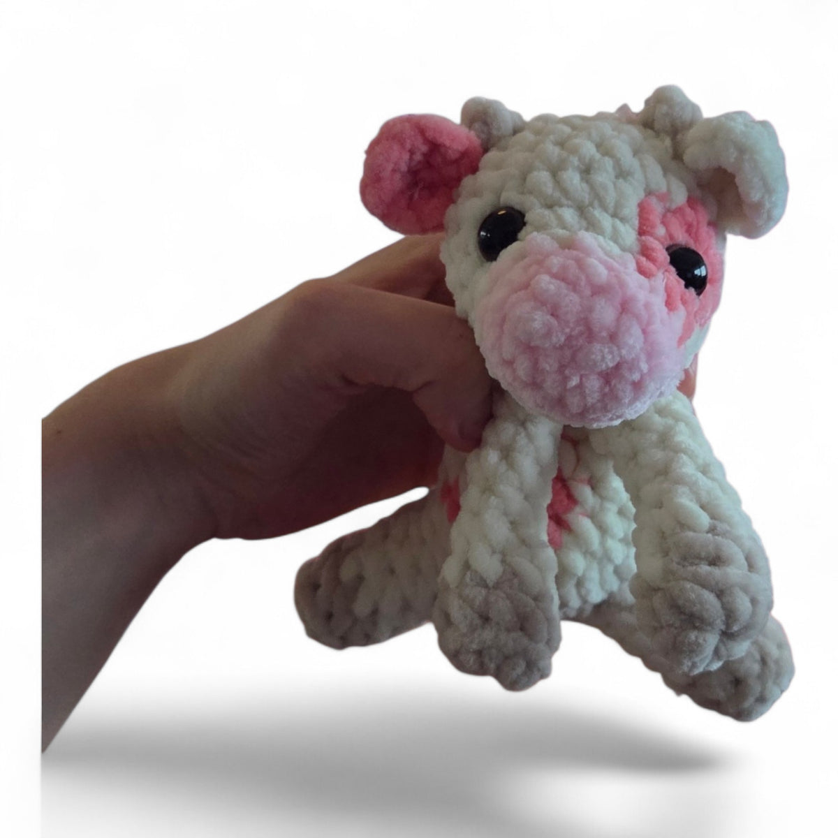 BrainRotPop handmade crochet cow plushie in cream and soft pink chenille yarn held in a hand